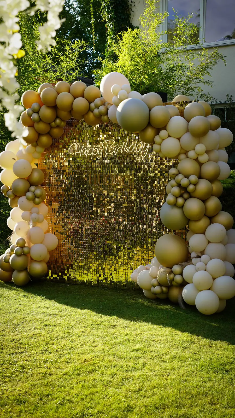 Outdoor gold sequin wall framed by a cream and gold balloon arch