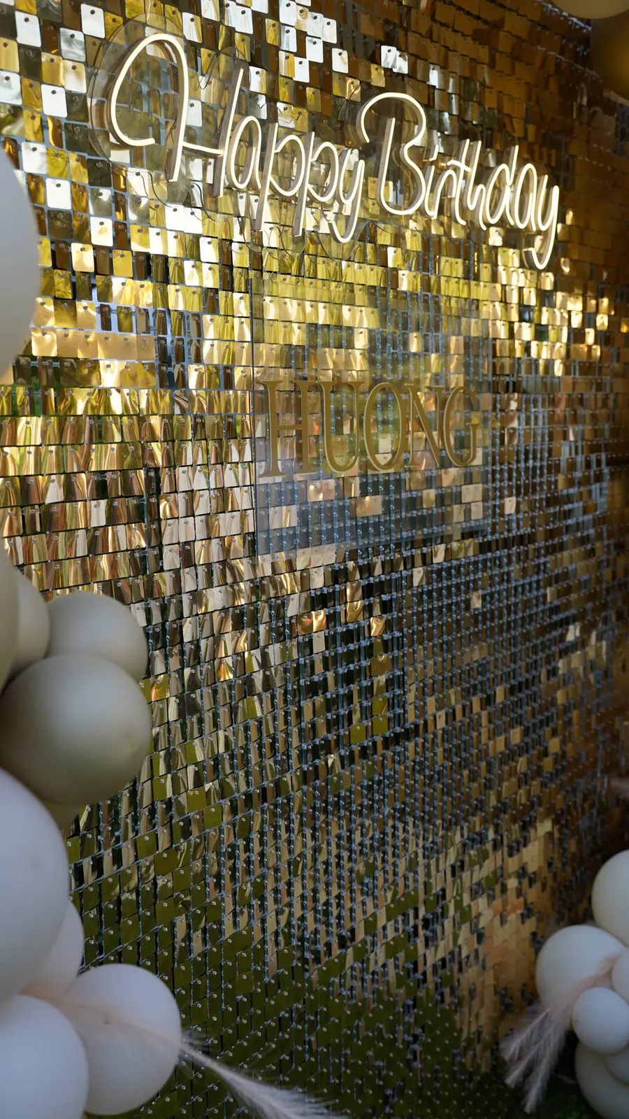 Gold sequin shimmer wall with a Happy Birthday neon and white balloons