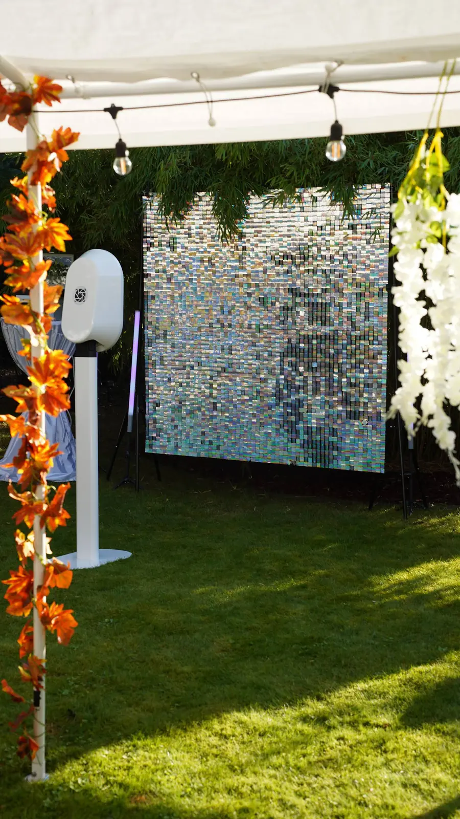 White booth on a lawn in front of an iridescent sequin backdrop