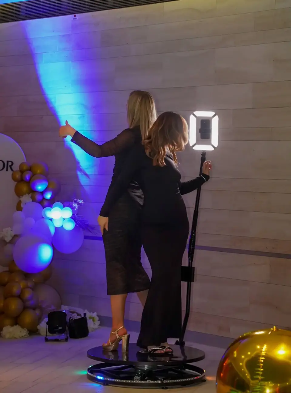 Two women in evening gowns posing on a 360° platform with blue accent lighting