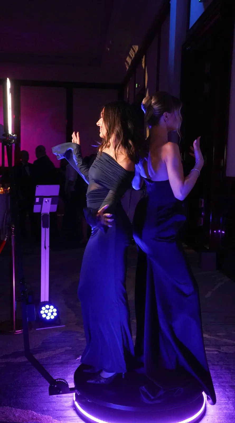 Two women in evening gowns posing on a 360° platform with a purple LED ring