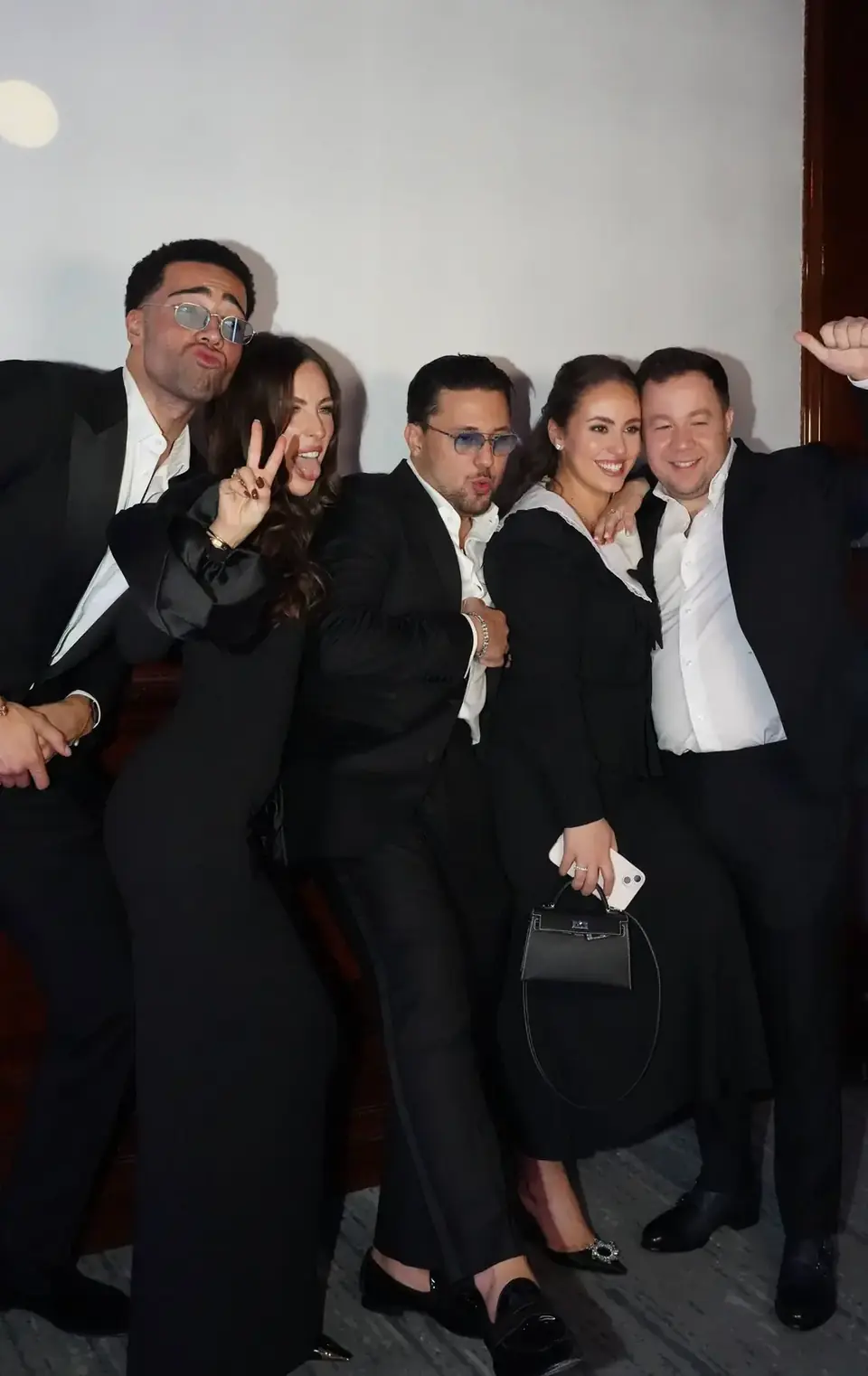 Five guests in black-tie attire posing playfully for a photo booth