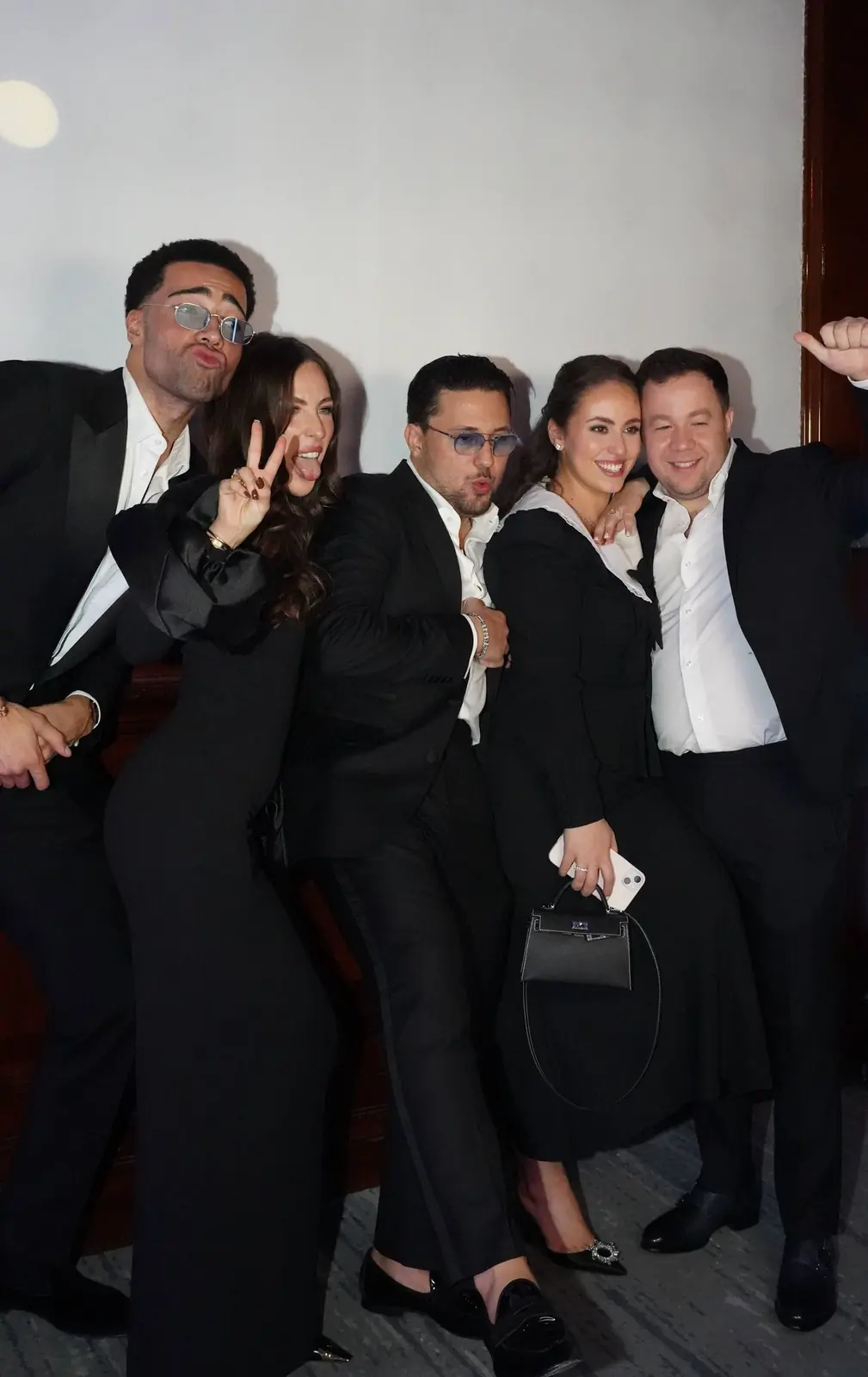 Five guests in black-tie attire posing playfully for a photo booth