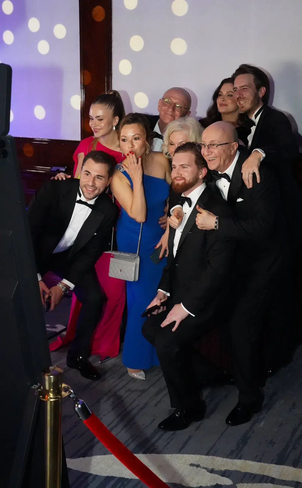A black-tie group smiling and posing in front of a photo booth at a gala