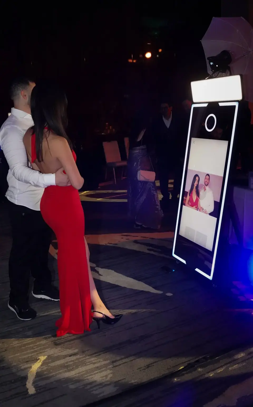 A couple in a red dress and formal wear using a glowing full-length mirror booth