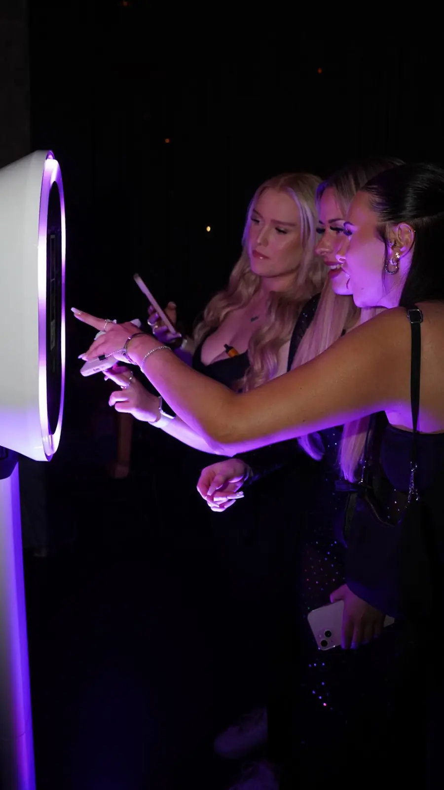 Three guests in evening wear using a white booth with a glowing purple ring light
