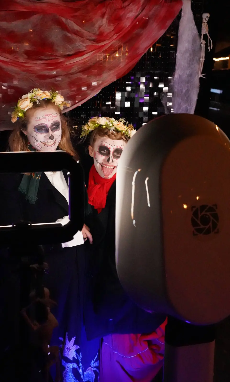 Guests with sugar-skull makeup posing at an illuminated white photo booth