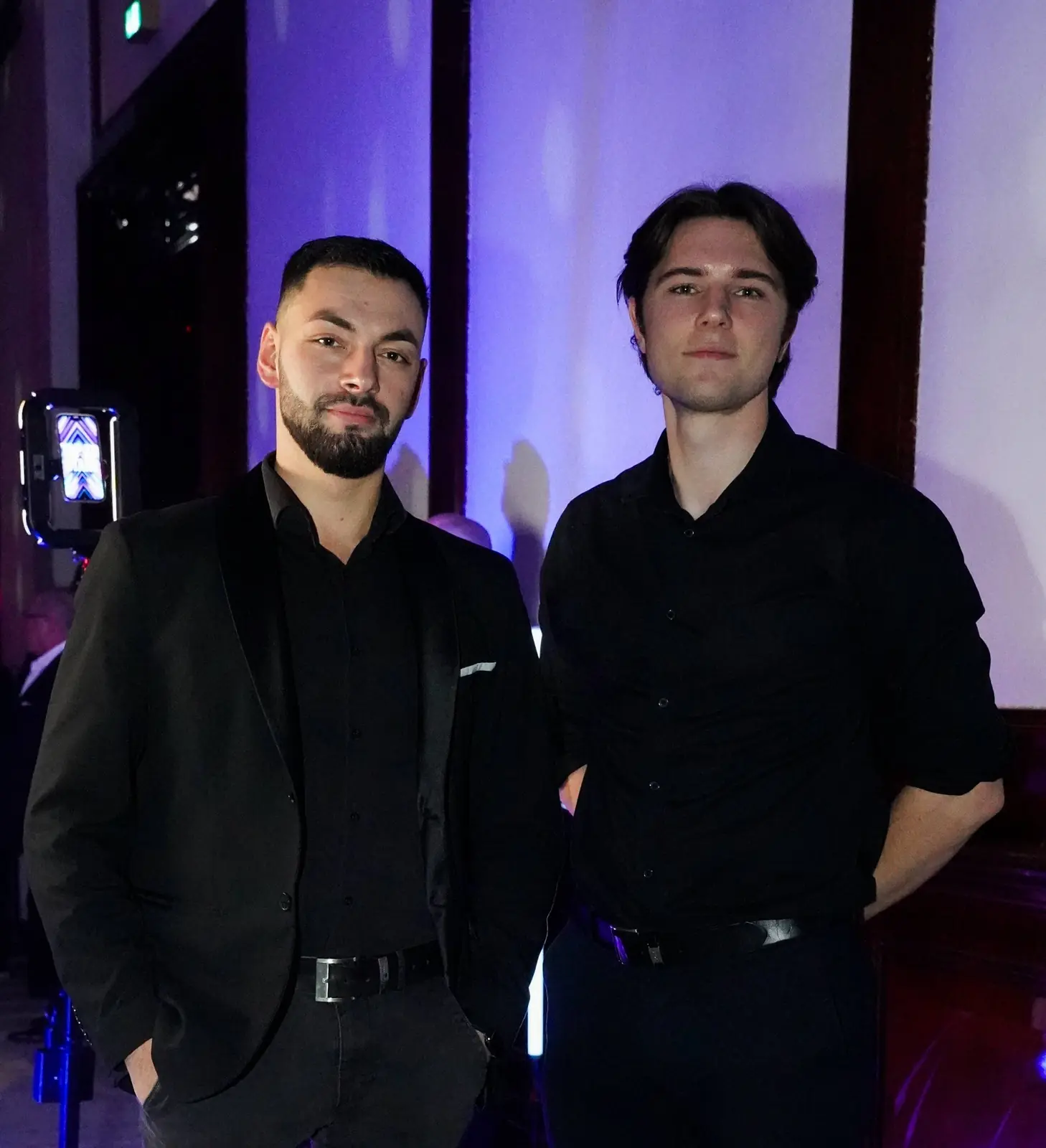 Two guests in black posing with a ring-light booth visible behind them